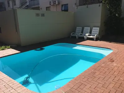 a blue swimming pool on a brick floor with chairs at Vilaroux in Stellenbosch