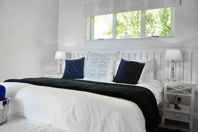 a white bedroom with a large bed with blue pillows at The Blue Marine Self-Catering in Gordonʼs Bay