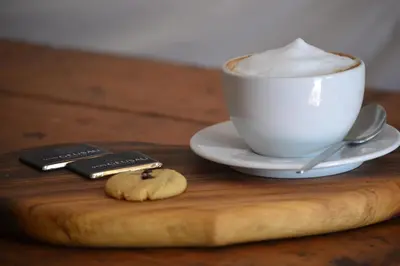 a cup of coffee and a cookie on a wooden tray at Via's Guesthouse in Greyton