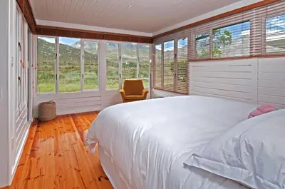 a bedroom with a bed and windows and a chair at Moon River House in Pringle Bay