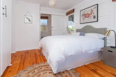a white bedroom with a large white bed and wooden floors at Moon River House in Pringle Bay