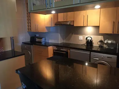 a kitchen with wooden cabinets and a black counter top at Hibernian Towers 1802 Self Catering Accommodation Strand Western Cape South Africa in Strand