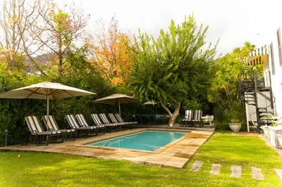 a swimming pool with chairs and umbrellas in a yard at Maison Chablis Guest House in Franschhoek