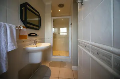 a white bathroom with a sink and a shower at Savoy Lodge in Cape Town