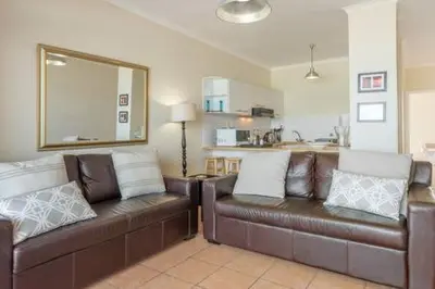 a living room with a brown leather couch and a kitchen at 325 Leisure Bay Cape Town in Cape Town