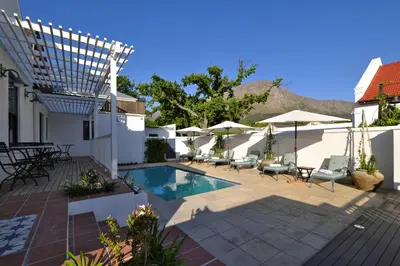a patio with a pool and chairs and umbrellas at Chapter House Boutique Hotel by The Living Journey Collection in Franschhoek