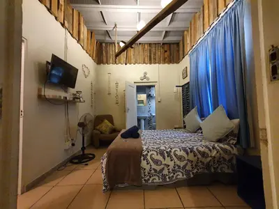 a bedroom with a bed with blue curtains and a tv at Bedrock Guest Studios in Strand