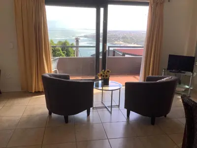 a living room with chairs and a table and a large window at Studio with unforgettable View in Gordonʼs Bay