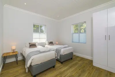 two beds in a room with white walls and wood floors at Irene Avenue Apartment with sea views in Somerset West