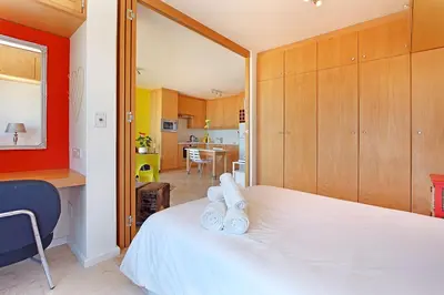 a bedroom with a white bed and a kitchen at Neptune Isle 214 in Cape Town