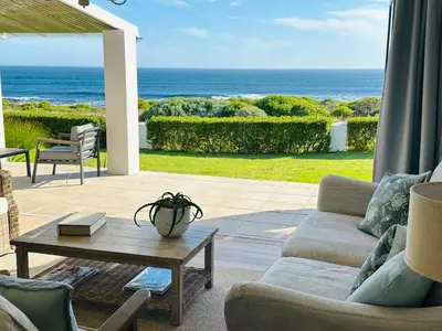a living room with a couch and a table and the ocean at Seapearl Oceanfront Villa and Cottage in Hermanus