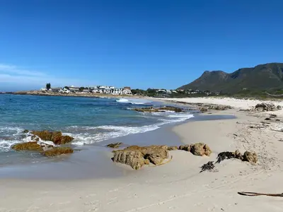 a beach with rocks in the sand and the ocean at Seapearl Oceanfront Villa and Cottage in Hermanus