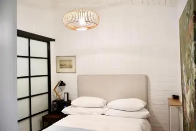 a bedroom with a bed with white sheets and a chandelier at Courtyard Studio lights and wi fi during load shedding in Stellenbosch