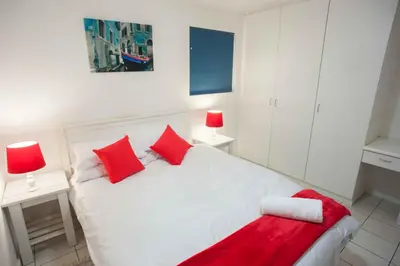 a bedroom with a white bed with red pillows at 20 Cayman Beach, Gordon's Bay in Gordonʼs Bay