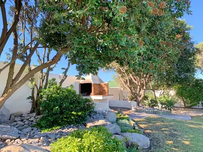 a garden with trees and rocks and a house at 63 Whalerock Estate in Hermanus