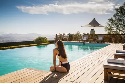 a woman in a bikini sitting next to a swimming pool at Delaire Graff Lodges and Spa in Stellenbosch