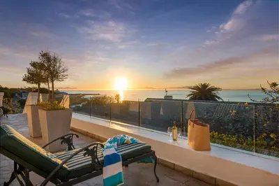 a balcony with a view of the ocean at sunset at Manor on the Bay in Gordonʼs Bay
