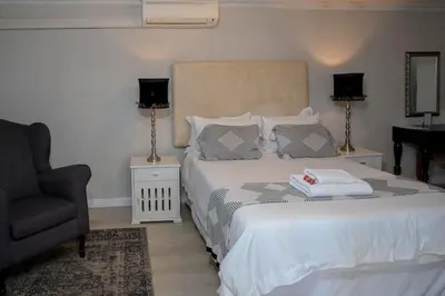 a bedroom with a white bed with a chair and a chair at Dark Chocolate Guest House in Durbanville