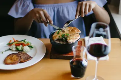 a person eating a sandwich with a bowl of food and a glass of wine at Zevenwacht Country Inn in Kuilsrivier