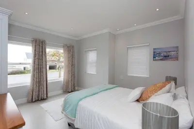 a white bedroom with a bed and a window at Coral Tree in Hermanus