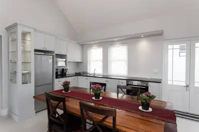 a white kitchen with a wooden table and chairs at Coral Tree in Hermanus