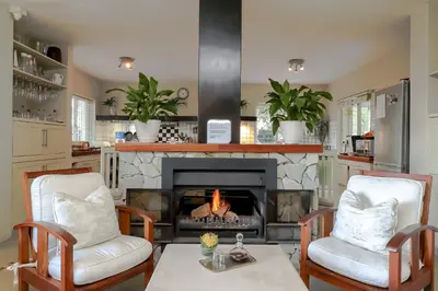 a living room with a fireplace with two chairs and a table at Hermanus Lodge on the Green - Solar Power in Hermanus