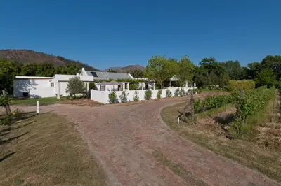 a dirt road leading to a white house at La Galiniere Guest Cottages in Franschhoek