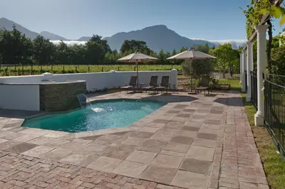 a swimming pool in a patio with chairs and umbrellas at La Galiniere Guest Cottages in Franschhoek