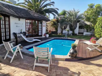 a swimming pool with chairs and a house at Pelican Place Guest Cottages in Durbanville