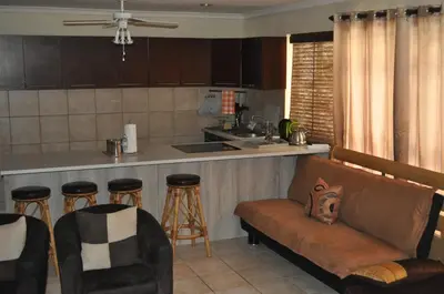 a living room with a couch and a kitchen at Pelican Place Guest Cottages in Durbanville