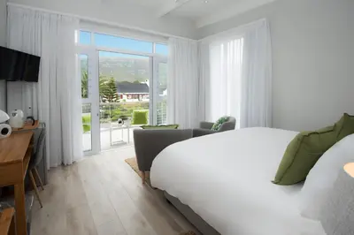a white bedroom with a bed and a balcony at Bamboo Guest House in Hermanus