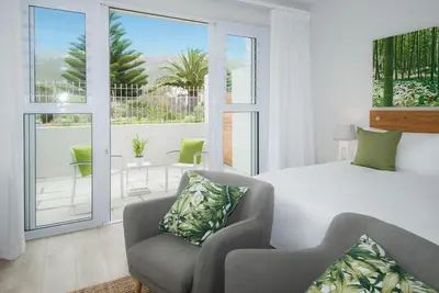 a bedroom with a bed and two chairs and a balcony at Bamboo Guest House in Hermanus