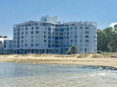a large white building on the beach near the water at False Bay Inn in Strand