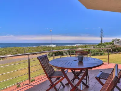 a table and chairs on a balcony with the ocean at Sandbaai Country House in Hermanus