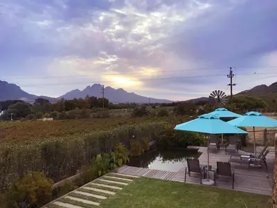 a patio with two blue umbrellas and a pond at Heuwelsig Farm Cottages in Franschhoek