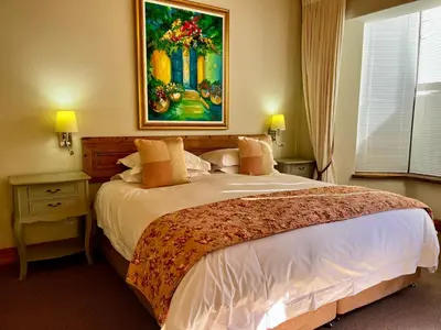 a bedroom with a large bed with a painting on the wall at Heuwelsig Farm Cottages in Franschhoek