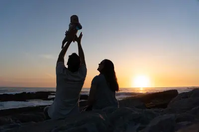a man and a woman sitting on the beach with a baby at Nothing But View in Hermanus