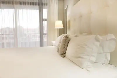 a white bed with white pillows and a window at Modern 2 bedroom with underground parking 1 mins from beach-205 La Cabina, Blouberg, Cape Town in Bloubergstrand