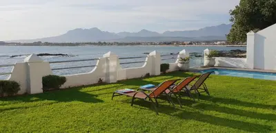 a yard with chairs and a swimming pool next to the water at Westbank Private Beach Villa, 4 Bedrooms, Private pool, on the Beach! in Gordonʼs Bay