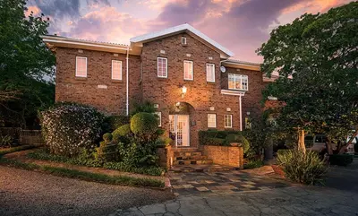 a large brick house with a sunset in the background at Leeuwenhof Guesthouse in Caledon