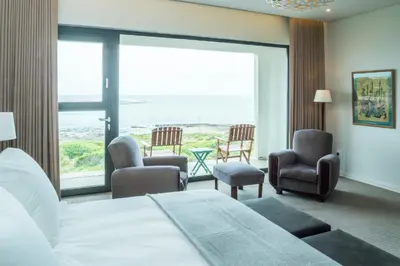 a hotel room with a bed and chairs and a large window at Schulphoek Seafront Boutique Hotel in Hermanus