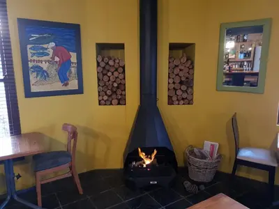 a fireplace in a restaurant with a table and chairs and a fire at Port Del Mar Guesthouse in Hermanus