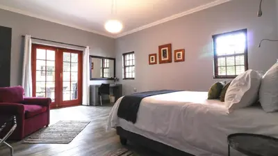 a bedroom with a bed and a chair and windows at Port Del Mar Guesthouse in Hermanus