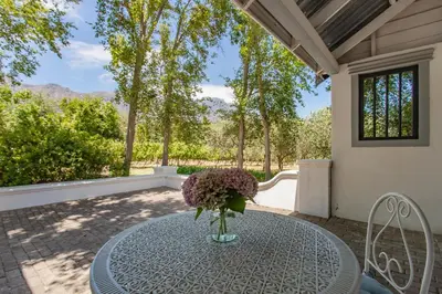 a vase of flowers on a table on a patio at Franschhoek Rose Cottages in Franschhoek