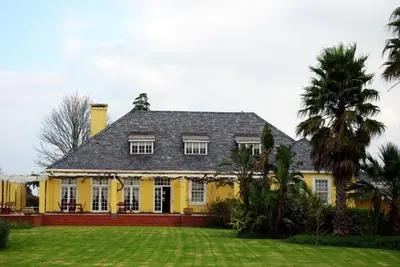 a yellow house with a black roof and a yard at Lyngrove Wines & Guesthouse in Stellenbosch