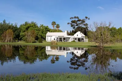 a white house sitting next to a lake at Sanddrif Stellenbosch Guest Farm in Stellenbosch