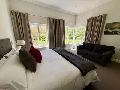 a bedroom with a bed and a chair and windows at Charming Villa in Stellenbosch