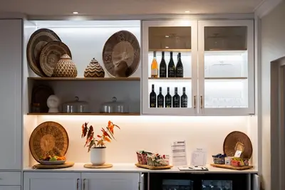 a kitchen with white cabinets with plates and wine bottles at Eikendal Lodge in Stellenbosch