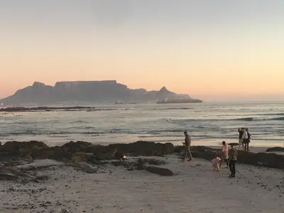 a group of people on the beach with table mountain in the background at Zeezicht 303 in Bloubergstrand