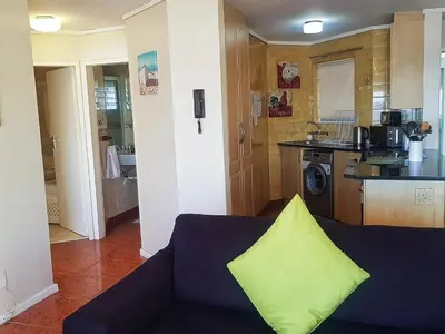 a living room with a blue couch with a yellow pillow at Zeezicht 303 in Bloubergstrand